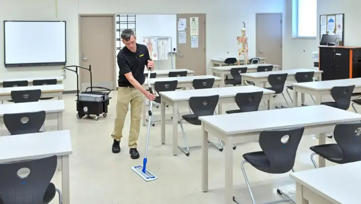 Person cleaning a room with a mop in a classroom or office space