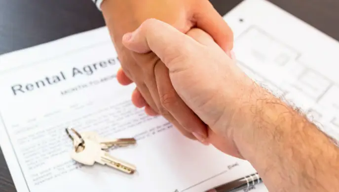 Two people shaking hands over signed paperwork