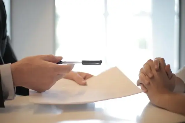 Two peoples hands across a desk, one holding a document and pen