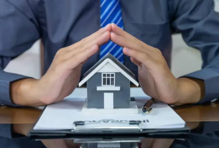 Man protecting house model with his hands over documents on a desk